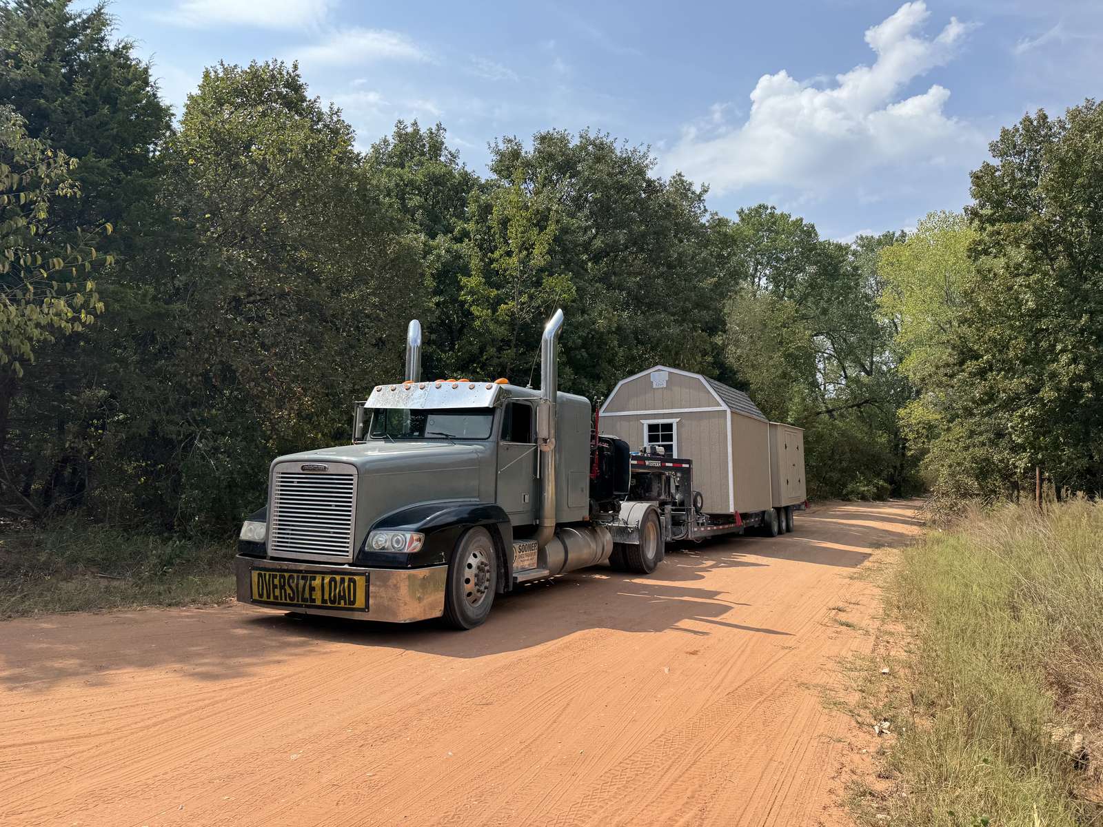 Tan lofted barn hauled down a red dirt road through the trees