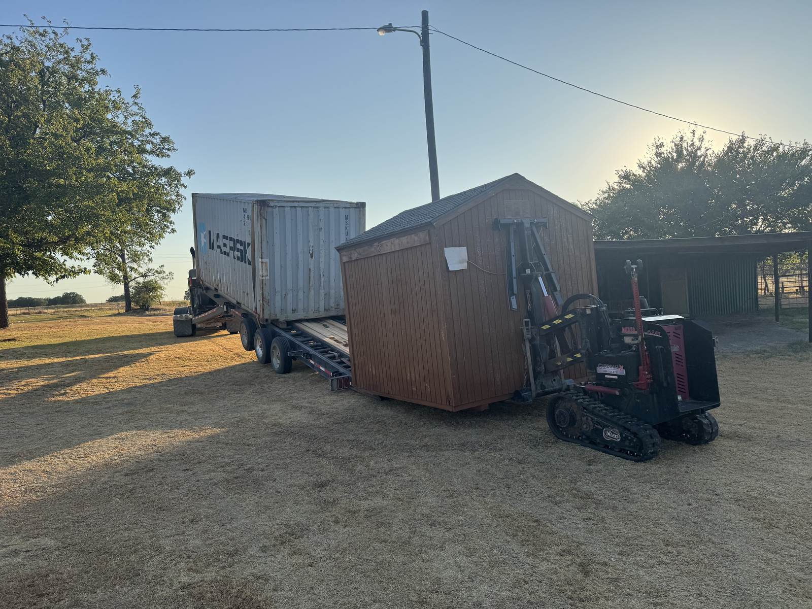 Maersk container on the trailer next to a wood shed on a crawler mover