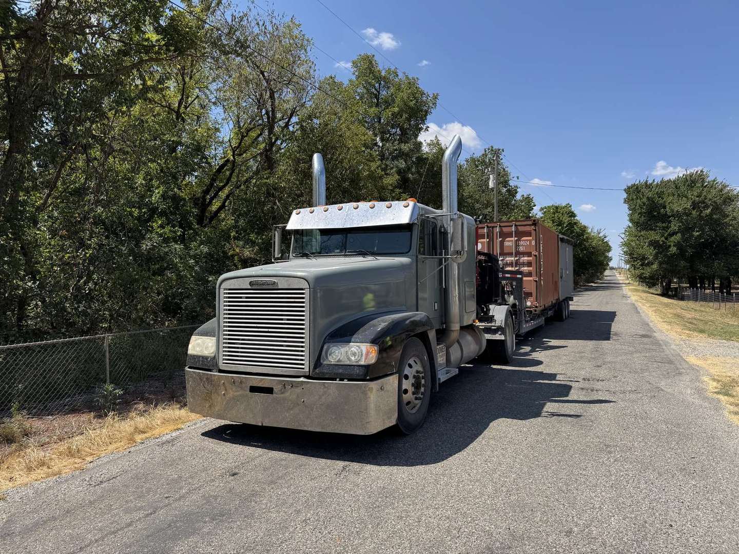 Truck hauling a rust-red shipping container down the road